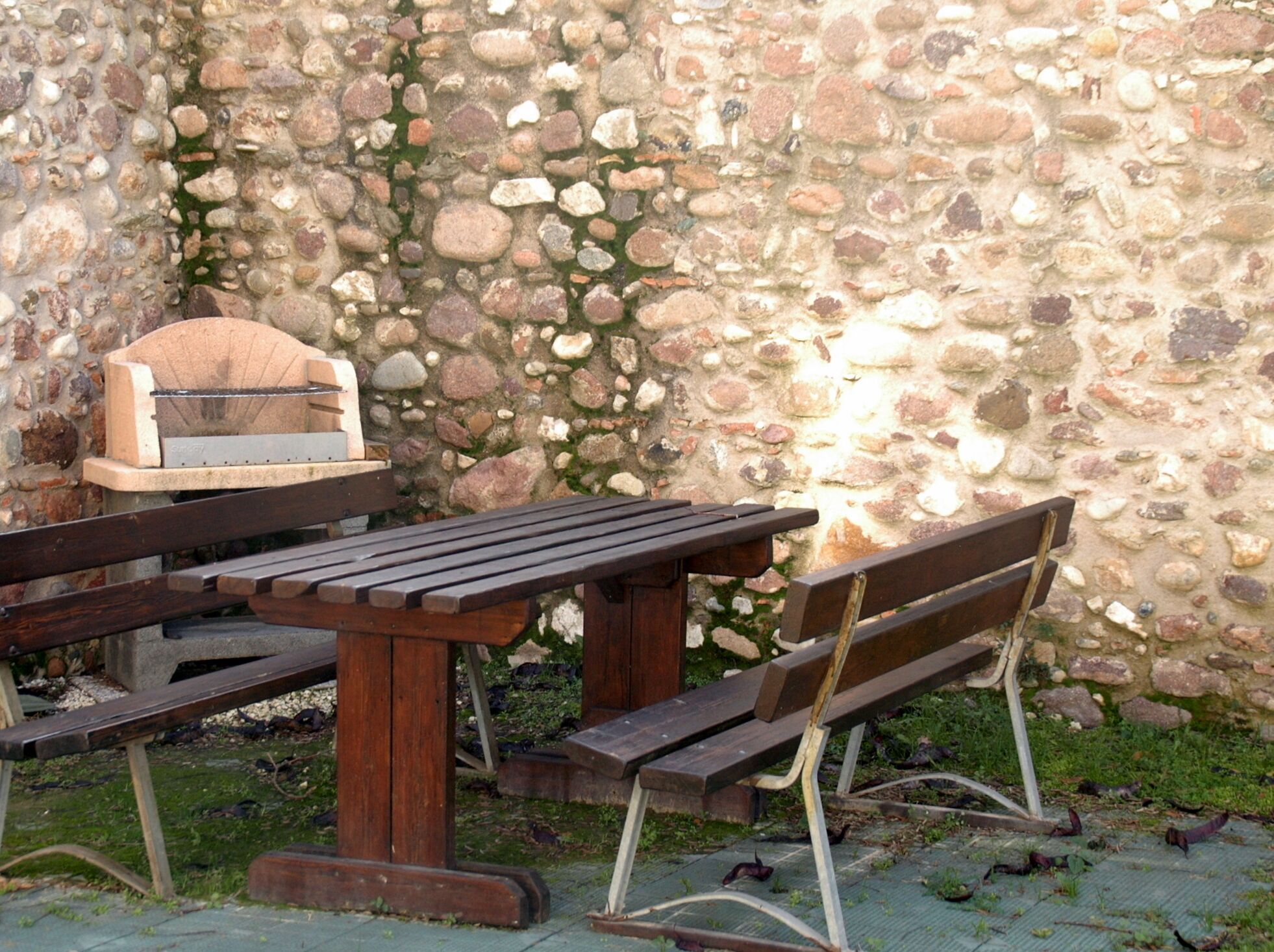 Conjunto de mesa e bancos de piquenique de madeira em frente a uma parede de pedra.