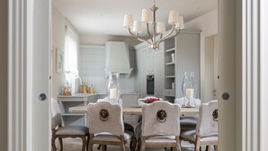 Un comedor con suelo de mármol, una araña y una mesa dispuesta con sillas.