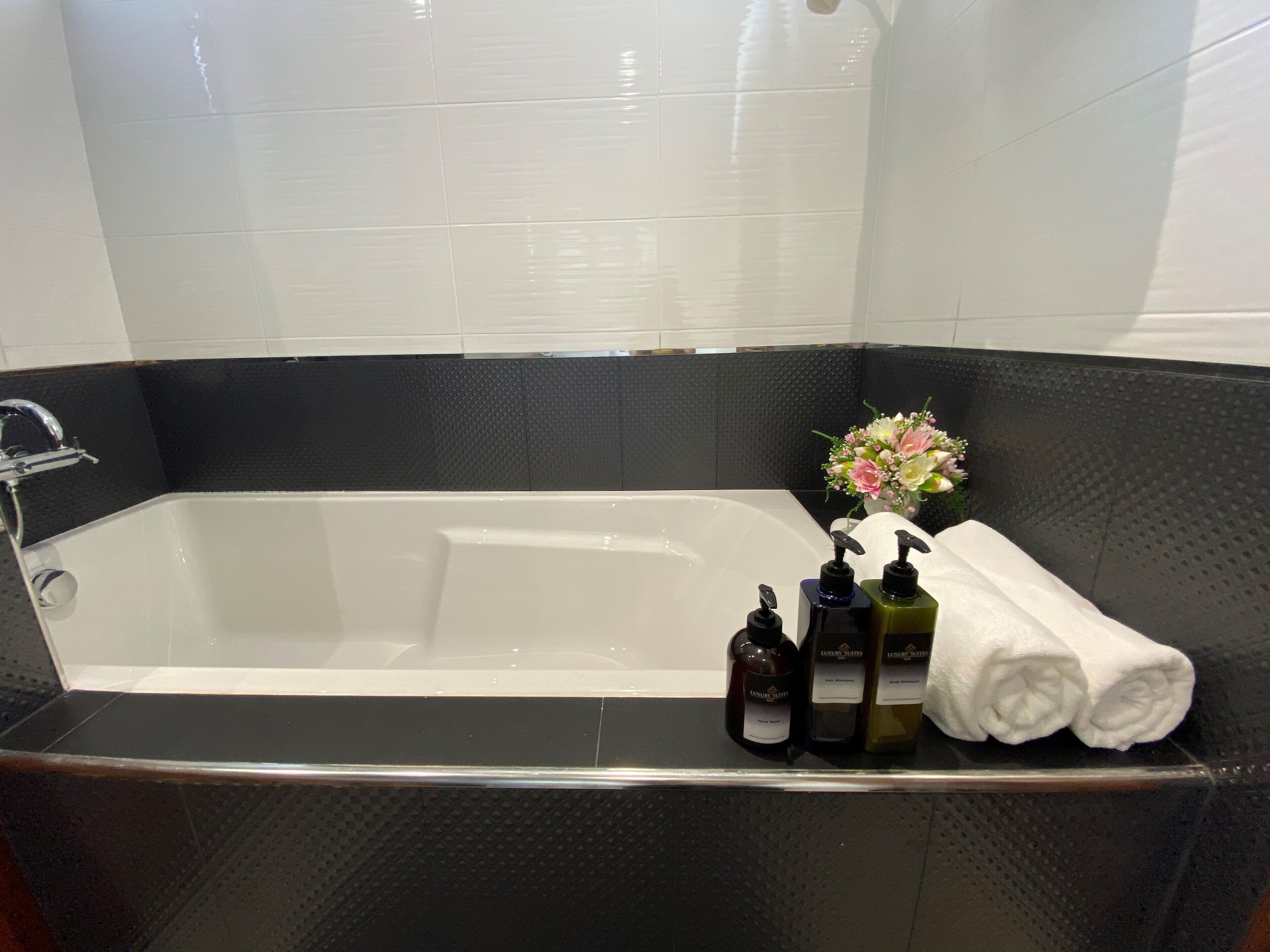 Un baño moderno con una bañera grande, paredes negras con textura, un área de ducha con azulejos blancos y un ramo de flores.