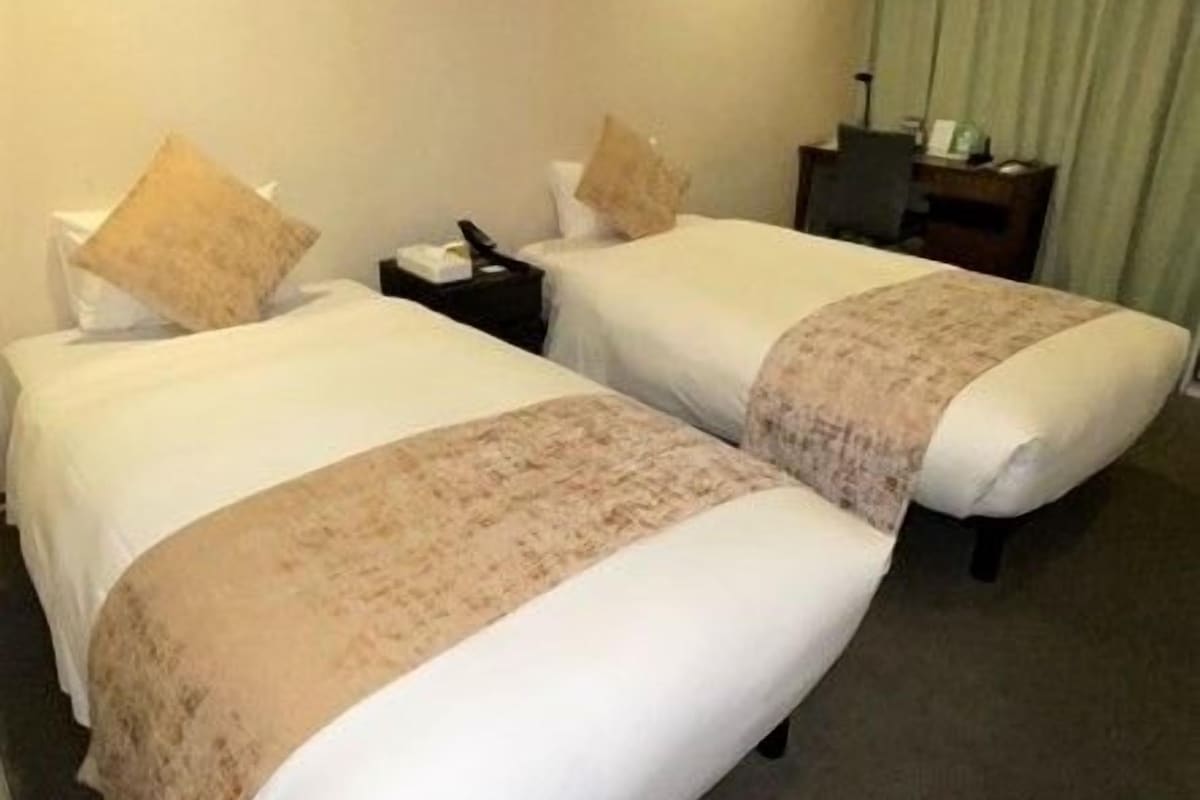 A hotel room with two beds, a desk, and a chair.
