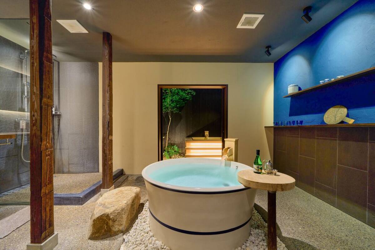 A modern bathroom with a large bathtub, a small round table with toiletries, and a blue wall with shelves.
