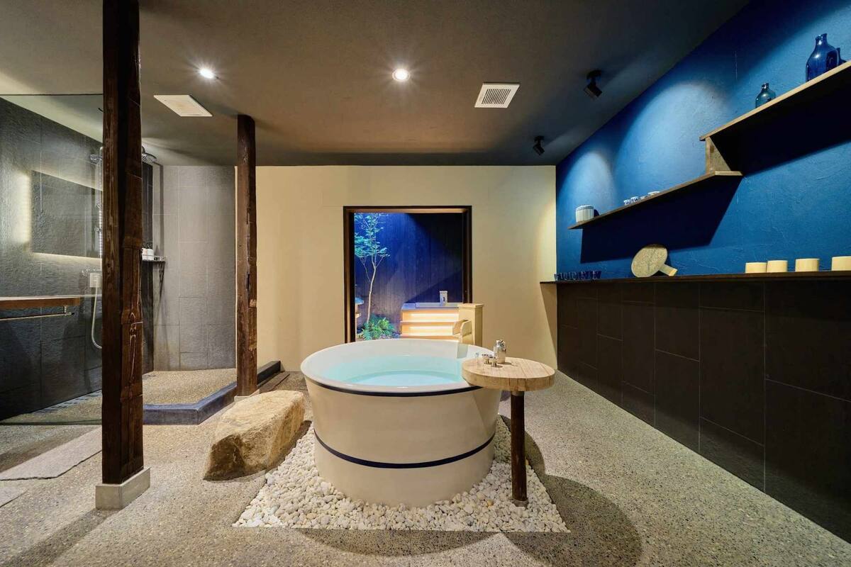 A modern bathroom with a freestanding bathtub, a small table with a cup and a bowl, and a shelf with toiletries.