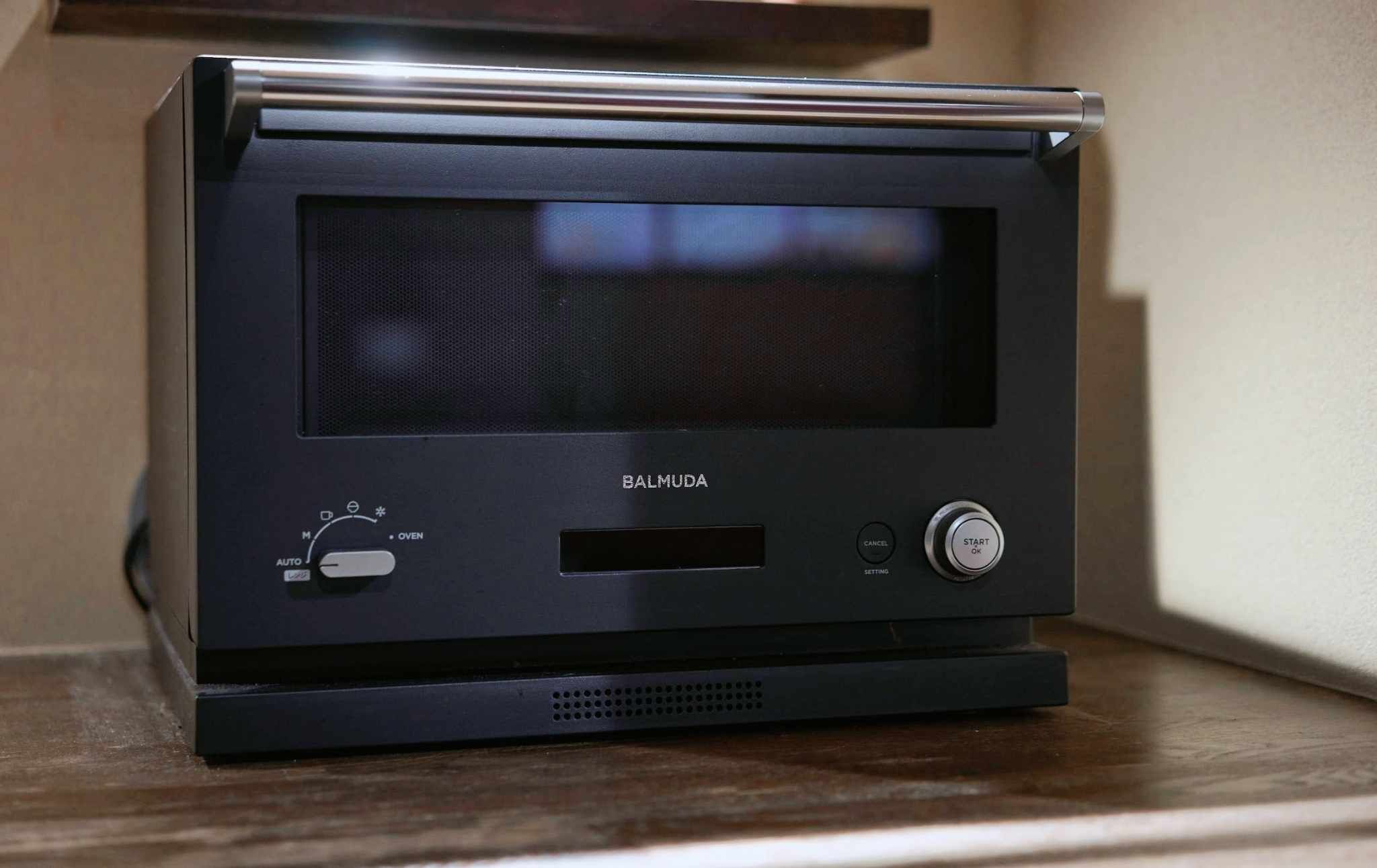A black Balmuda oven with a digital display, control knobs, and a start/stop button.