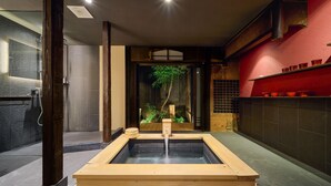 Ein traditionelles japanisches Onsen mit einer Holzplattform, einer Steinsäule und einem roten Regal mit Tassen.