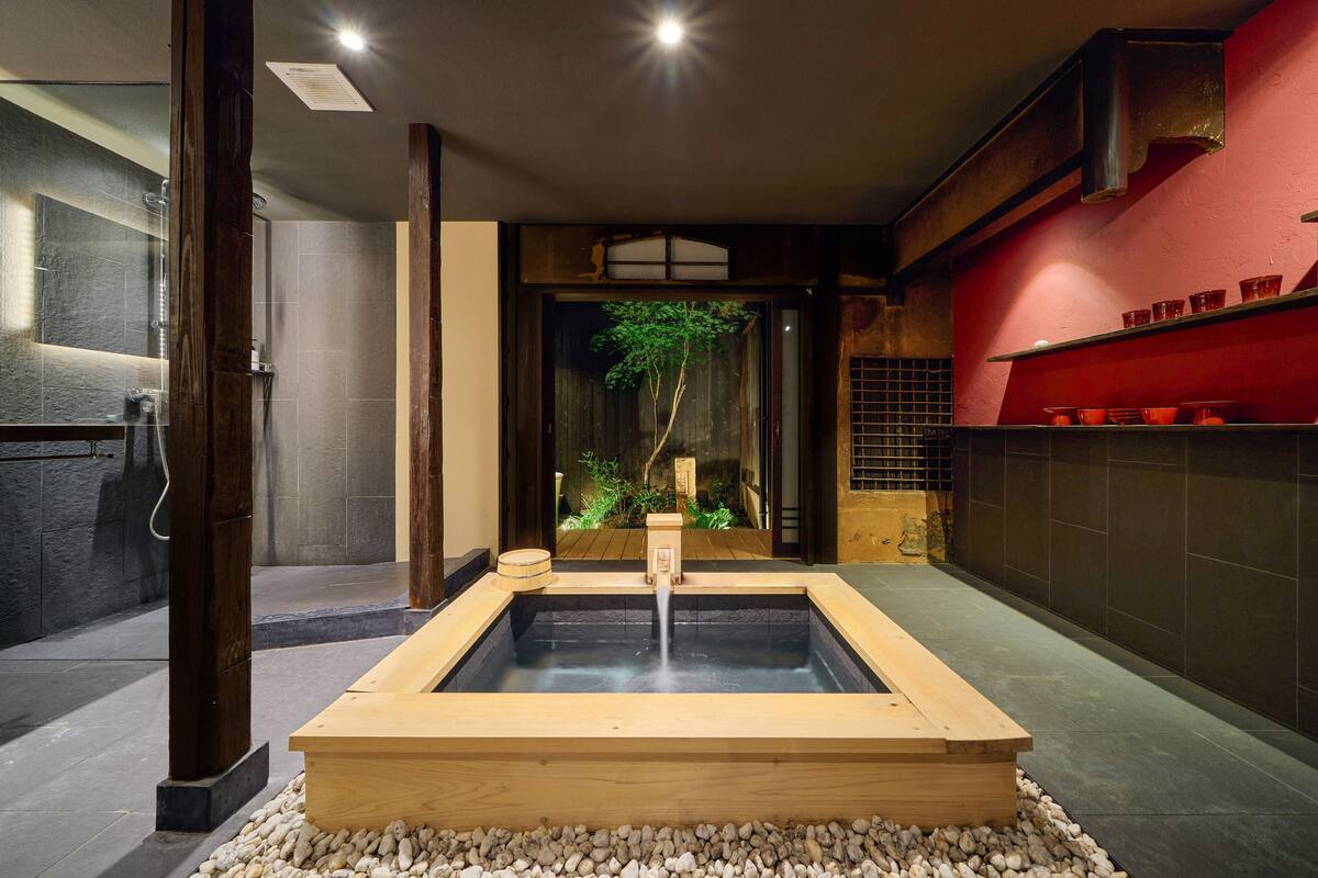 A traditional Japanese onsen with a wooden platform, a stone wall, and a red shelf with cups.