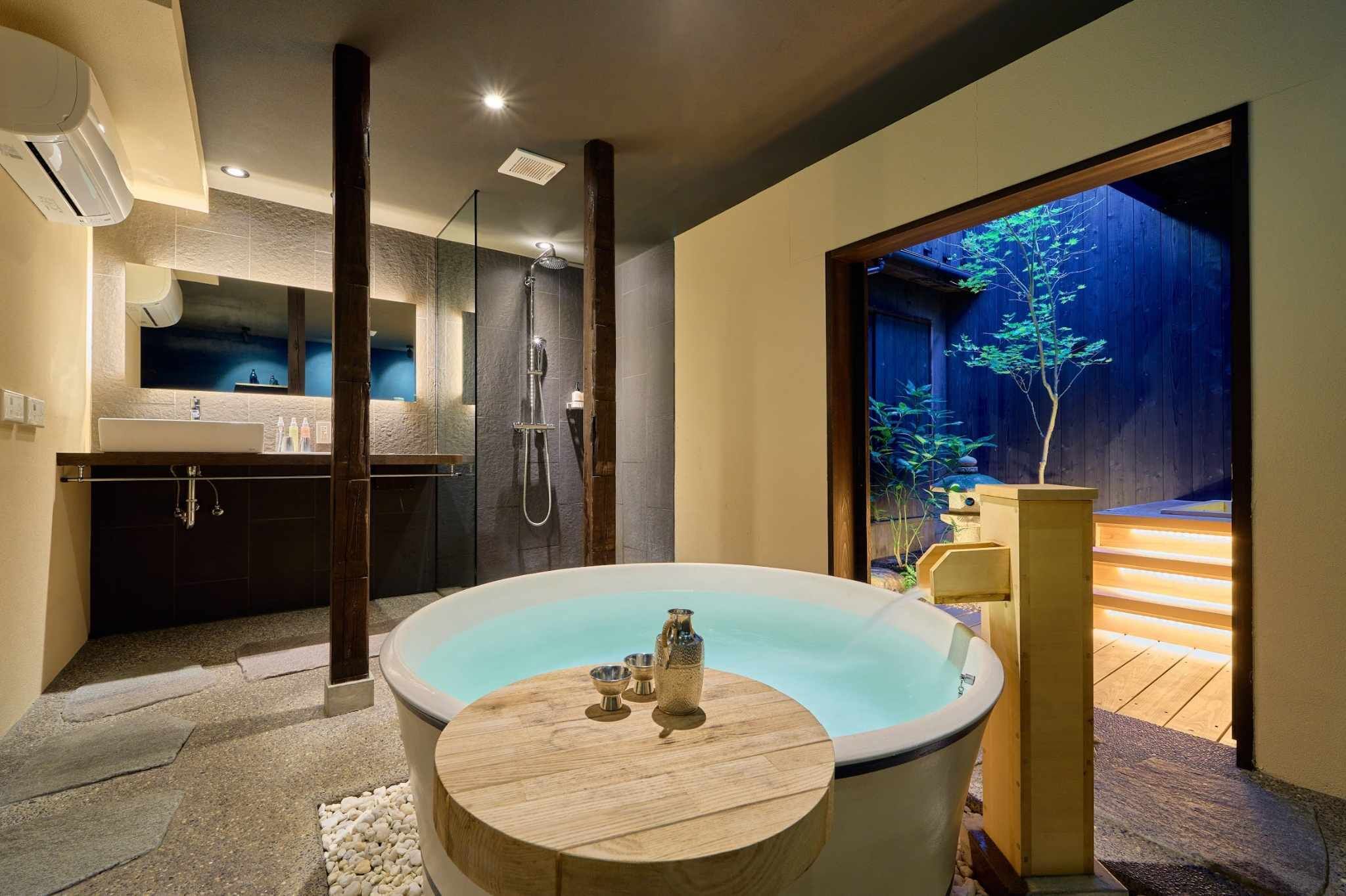 A modern bathroom with a large bathtub, a shower, and a wooden bench.