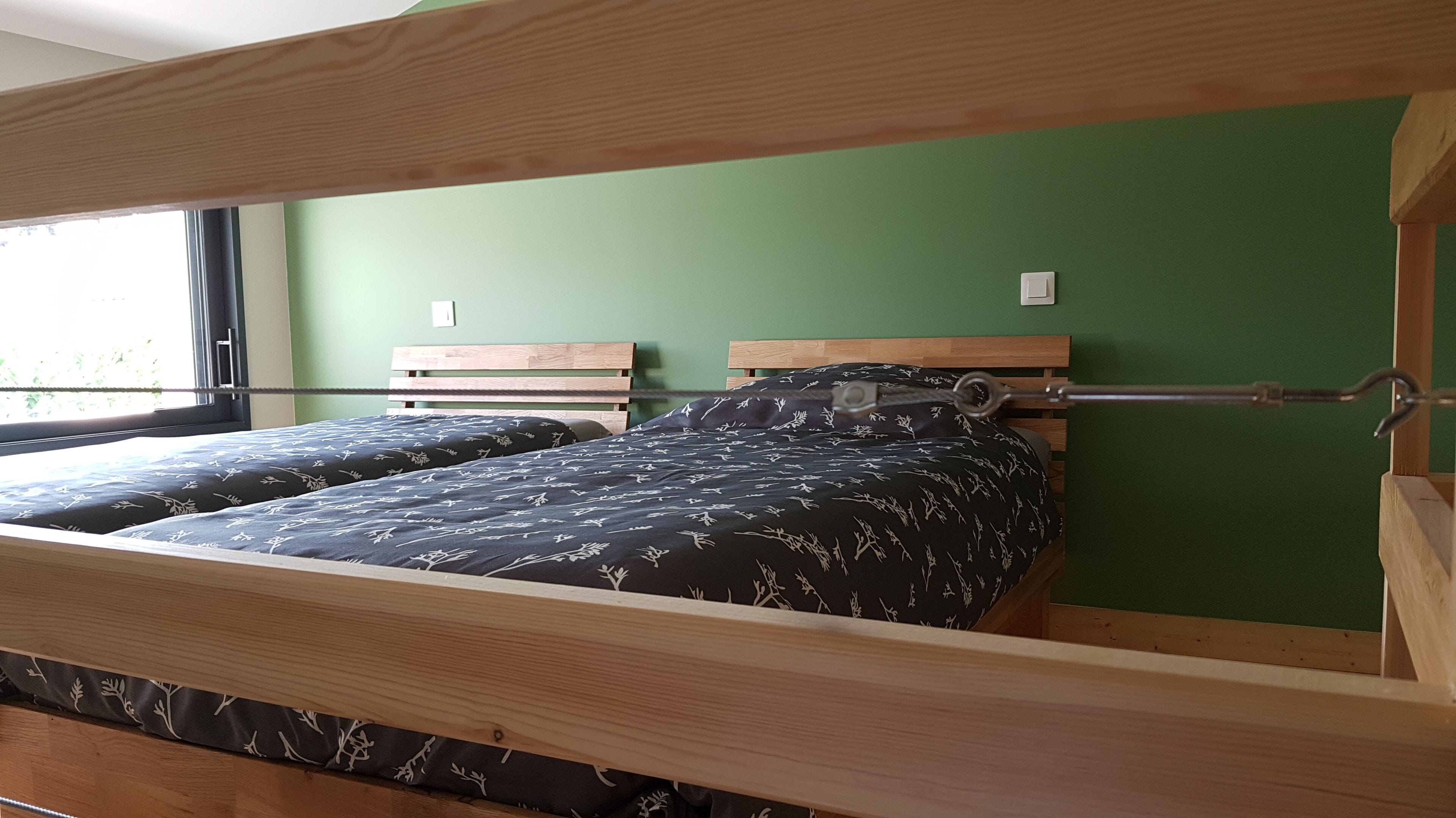 A bunk bed with a wooden frame, two pillows with a floral pattern, and a green wall.