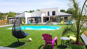 Una casa moderna con piscina, una hamaca y mobiliario exterior.