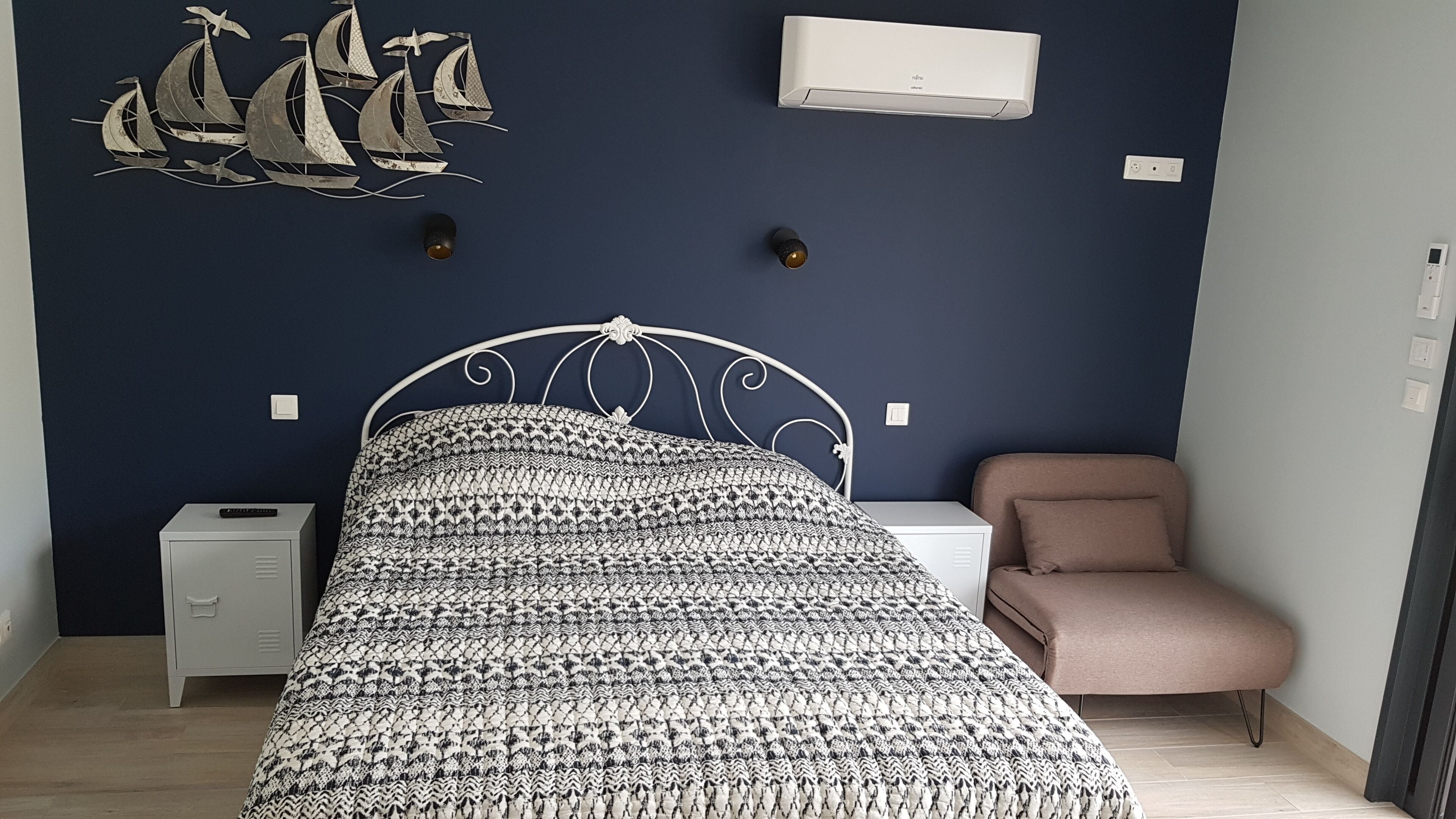 Une chambre à coucher comprenant un lit, une table de chevet, une commode, une chaise et un climatiseur fixé au mur.