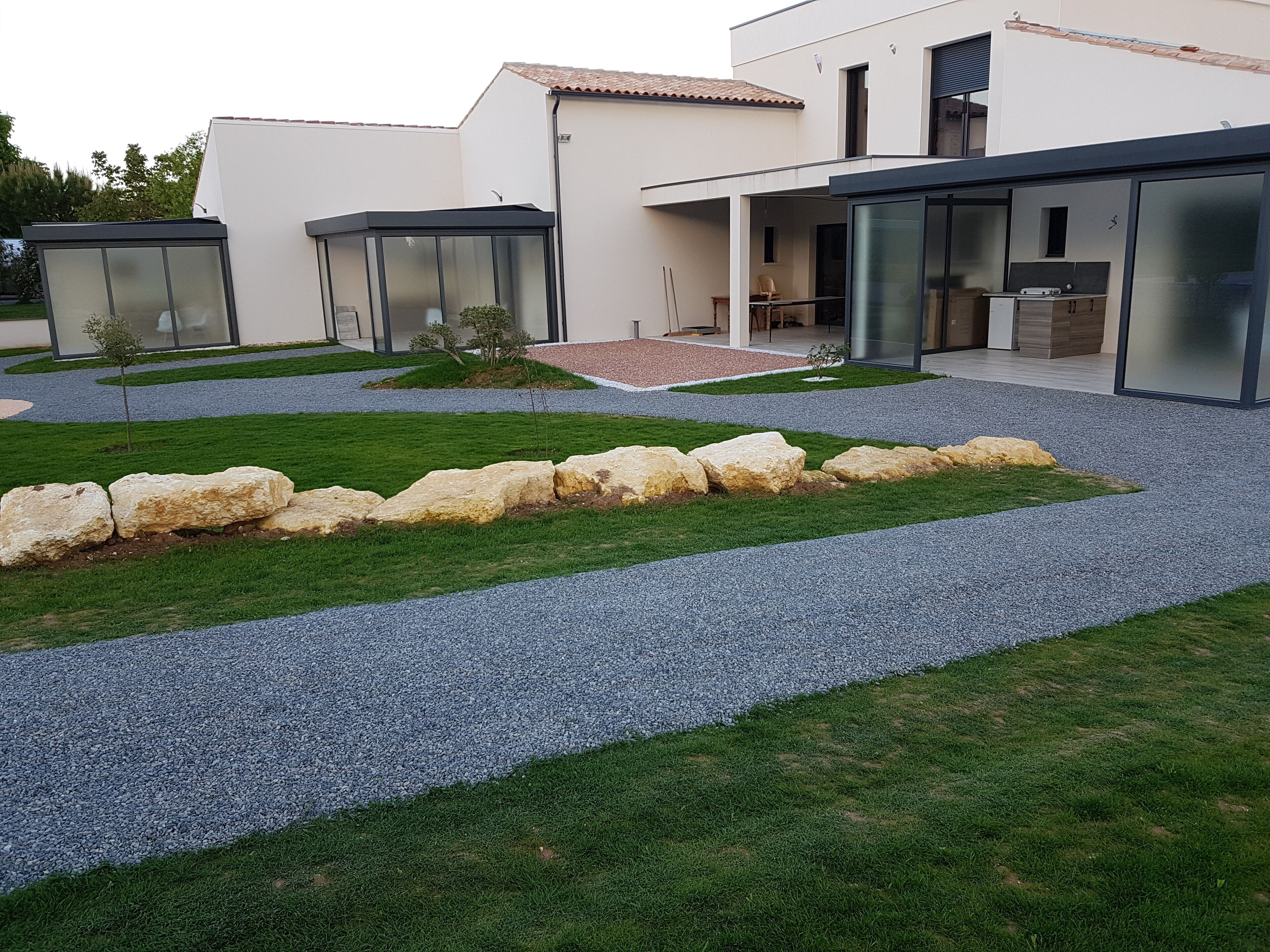 A modern house with a patio area, a gravel pathway, and a small garden with rocks and grass.