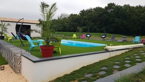 Un patio trasero con piscina, sillas coloridas y una palmera.