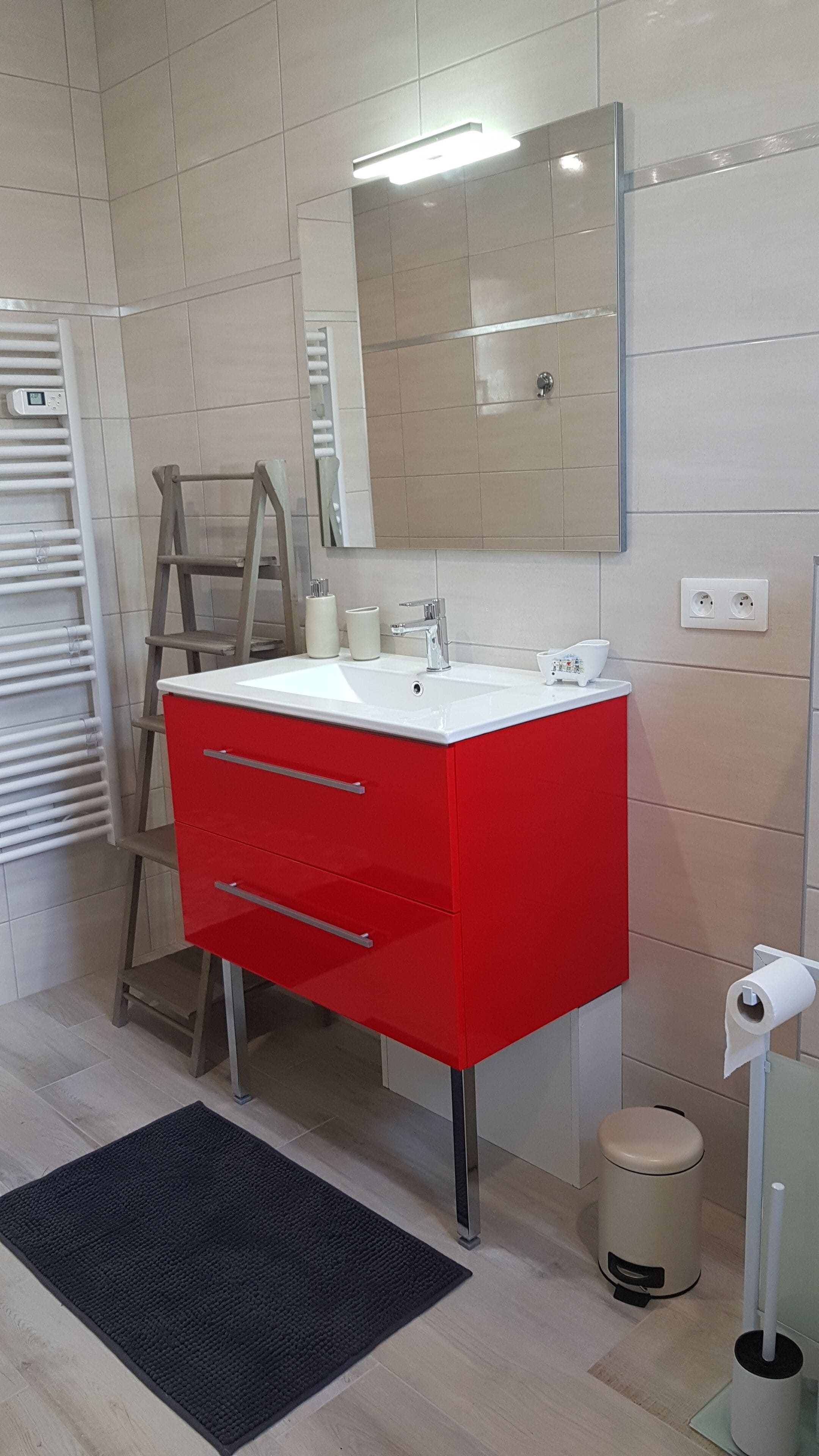 A bathroom with a red vanity, a mirror, a toilet, and a trash bin.