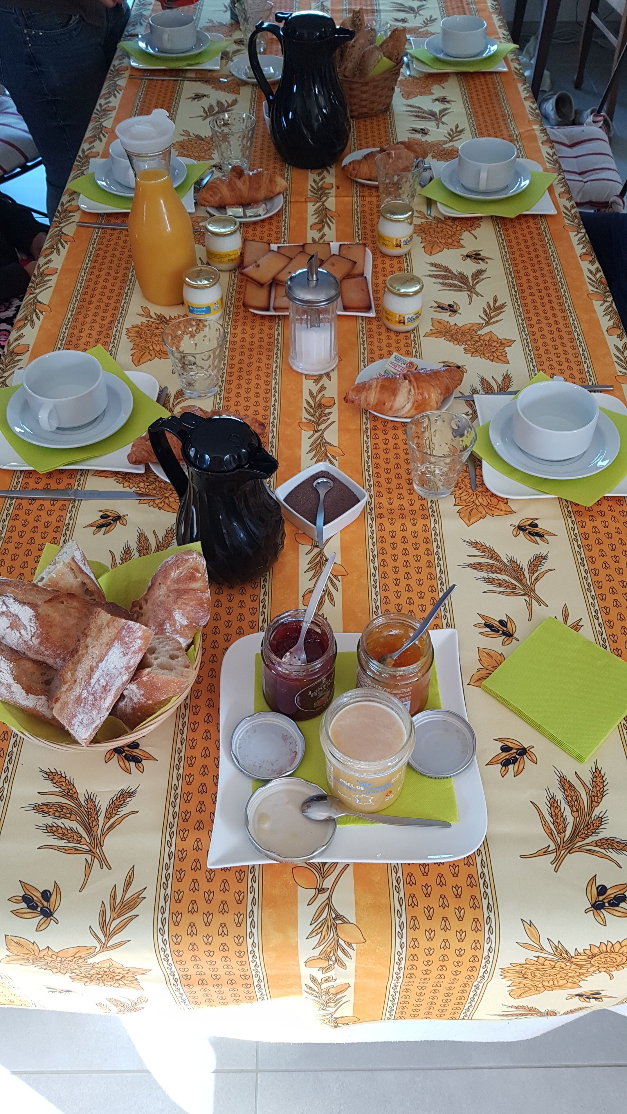 Mesa de desayuno dispuesta con pan, bollería, mermeladas y bebidas.