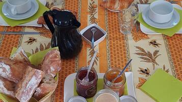Mesa de desayuno dispuesta con pan, bollería, mermeladas y bebidas.