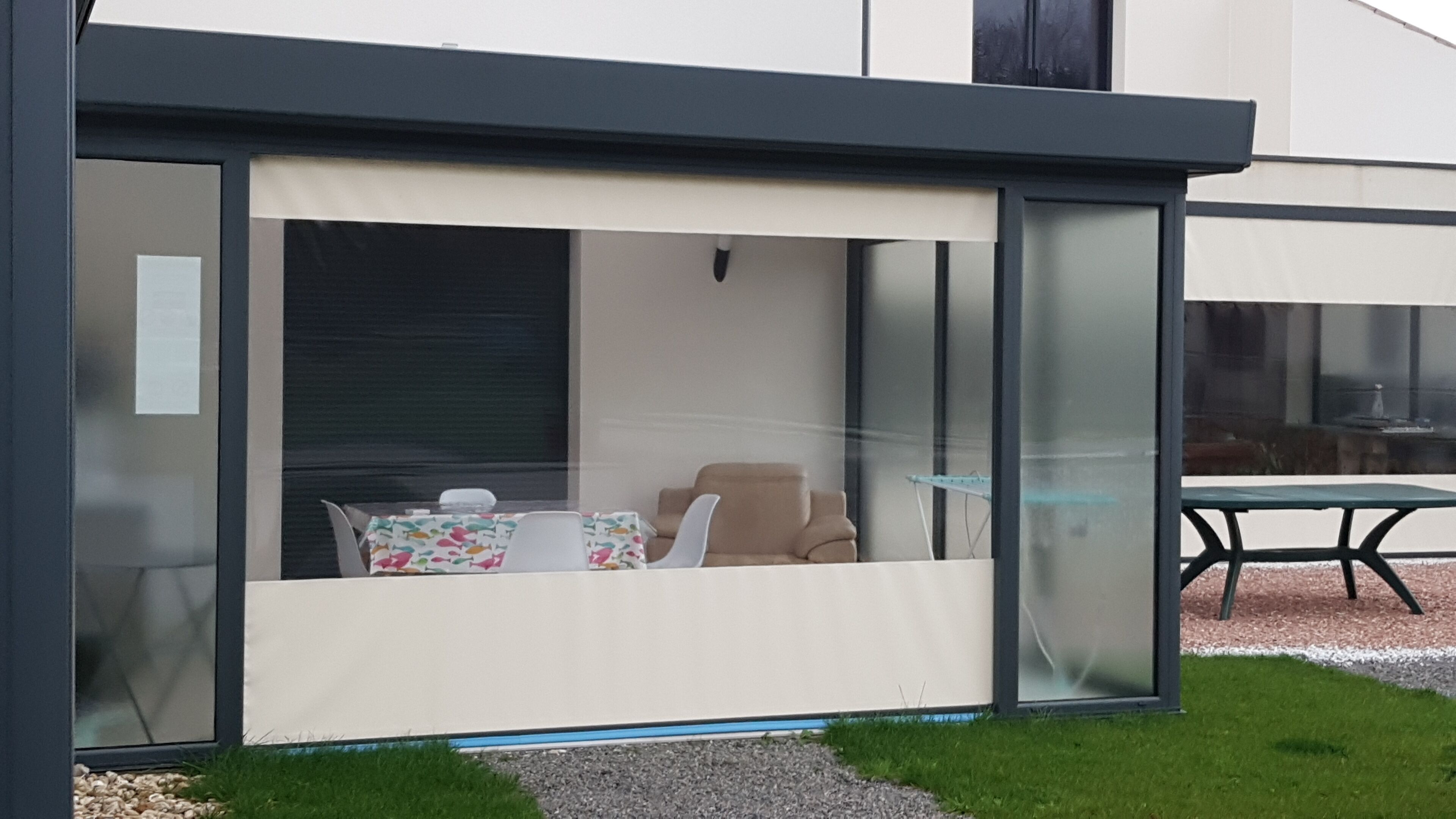 A modern outdoor seating area with a glass enclosure, a table, and a chair.