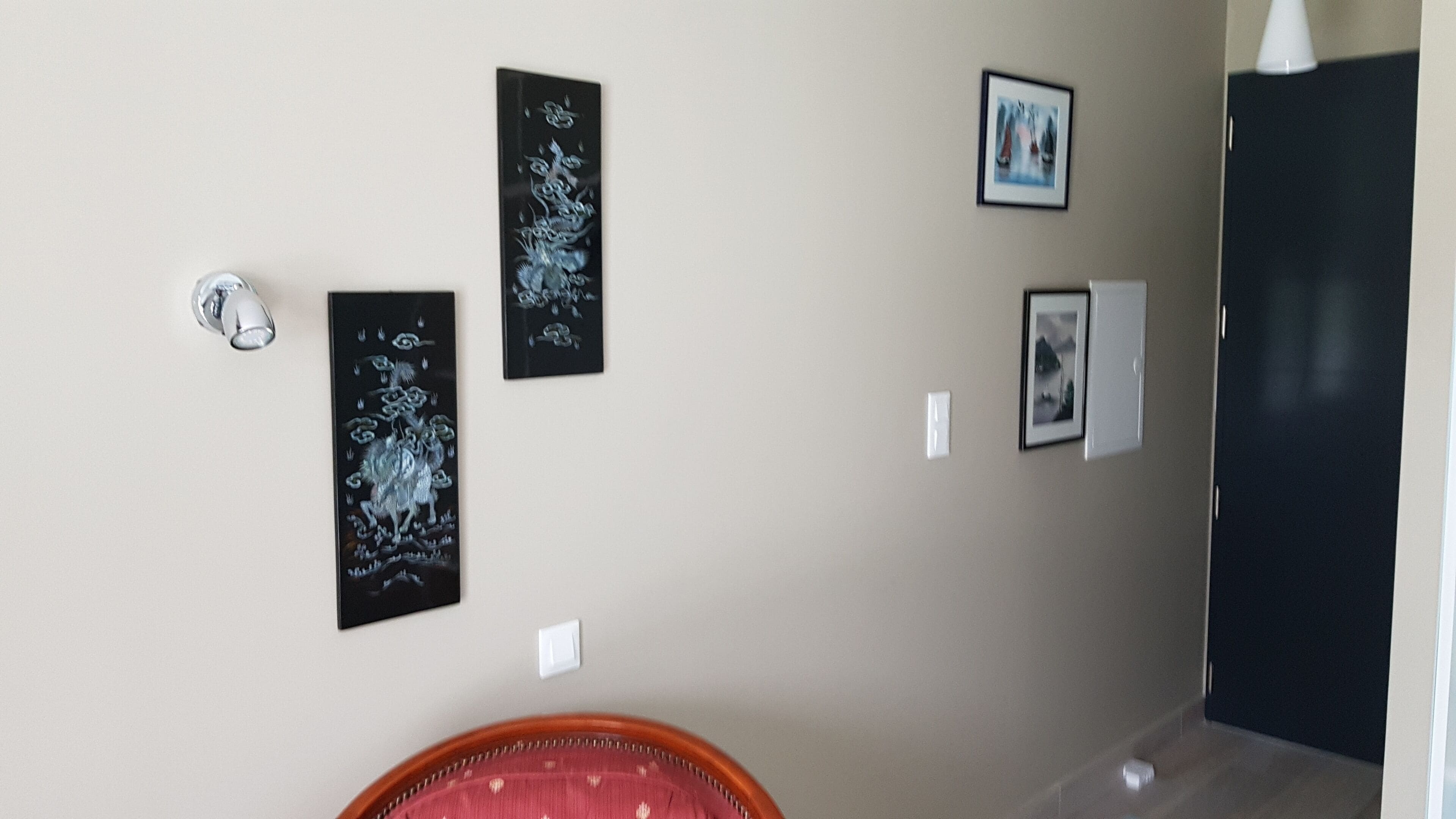 Un couloir avec une porte, un interrupteur et trois œuvres d’art encadrées accrochées au mur.