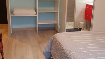 A bedroom with a bed, a wardrobe with multiple shelves, a small stool, and a red cabinet.