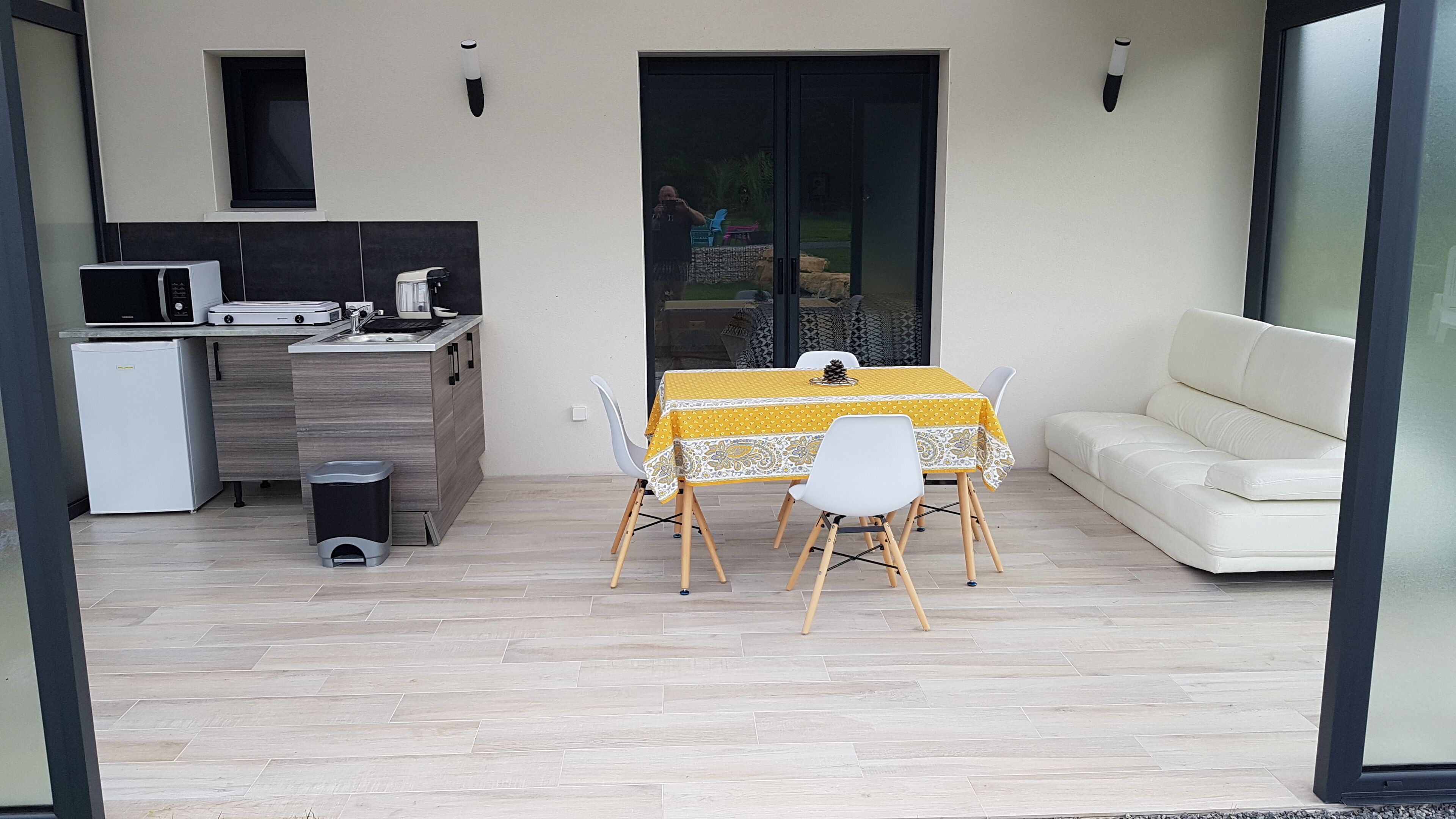 Une cuisine moderne équipée d’un four à micro-ondes, d’un grille-pain et d’un évier. On y trouve une table à manger avec des chaises et une nappe jaune. Un canapé blanc est placé contre le mur.