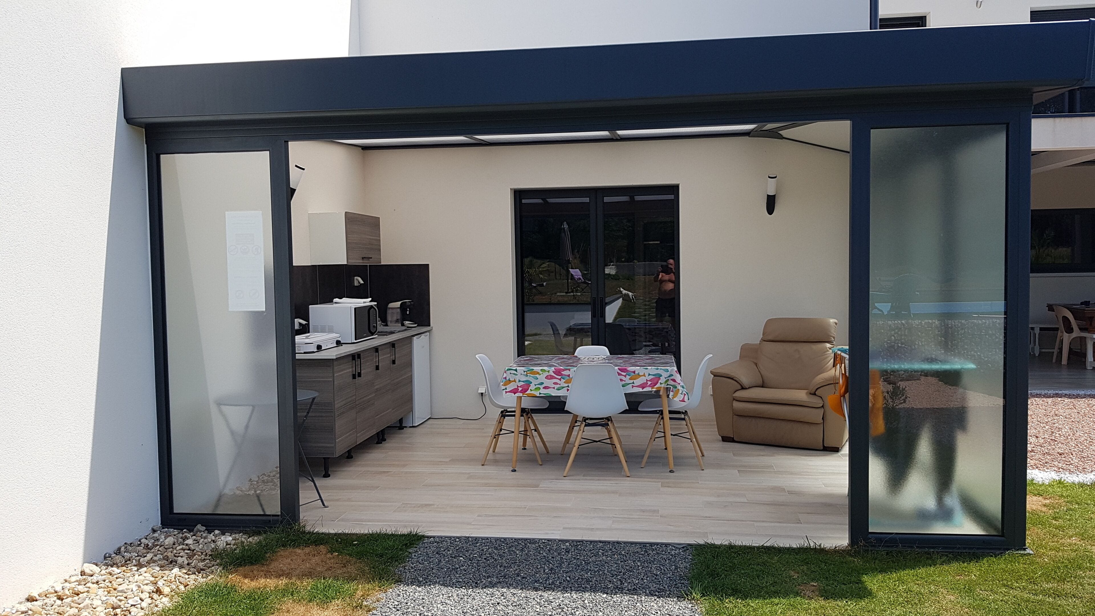 A modern outdoor dining area with a table and chairs, a sofa, and a kitchen area with appliances.