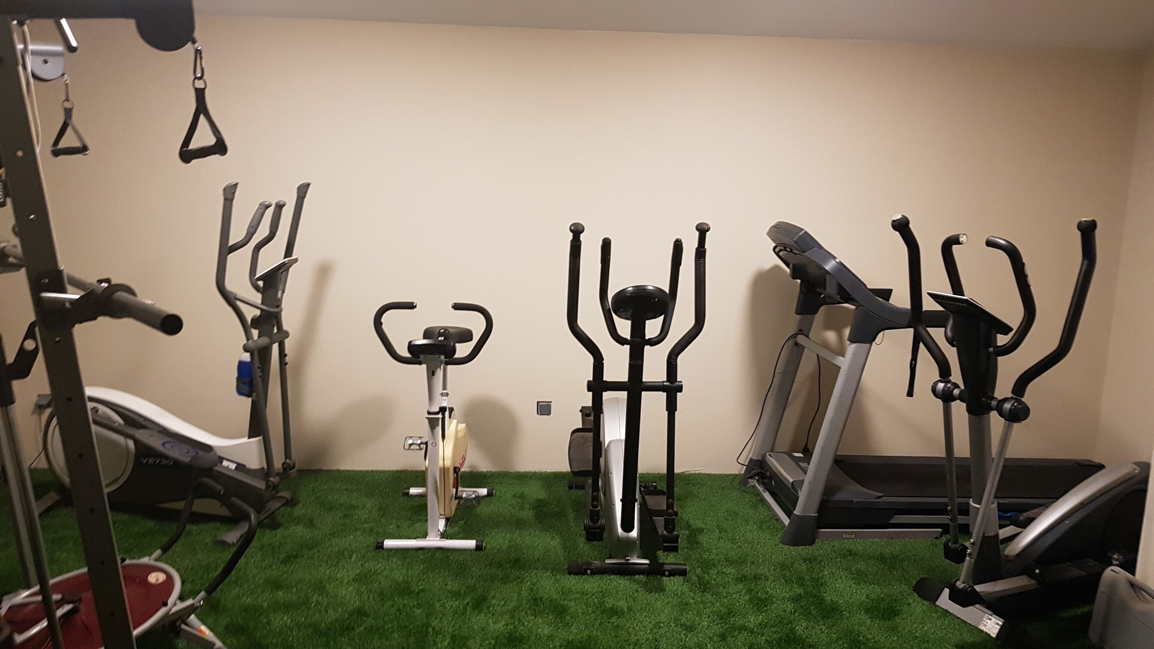 Ein Heimfitnessraum mit verschiedenen Trainingsgeräten, darunter ein Laufband, ein Crosstrainer und ein stationäres Fahrrad.