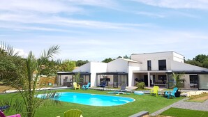 Una casa moderna de dos pisos con piscina, césped verde y zona de estar exterior.