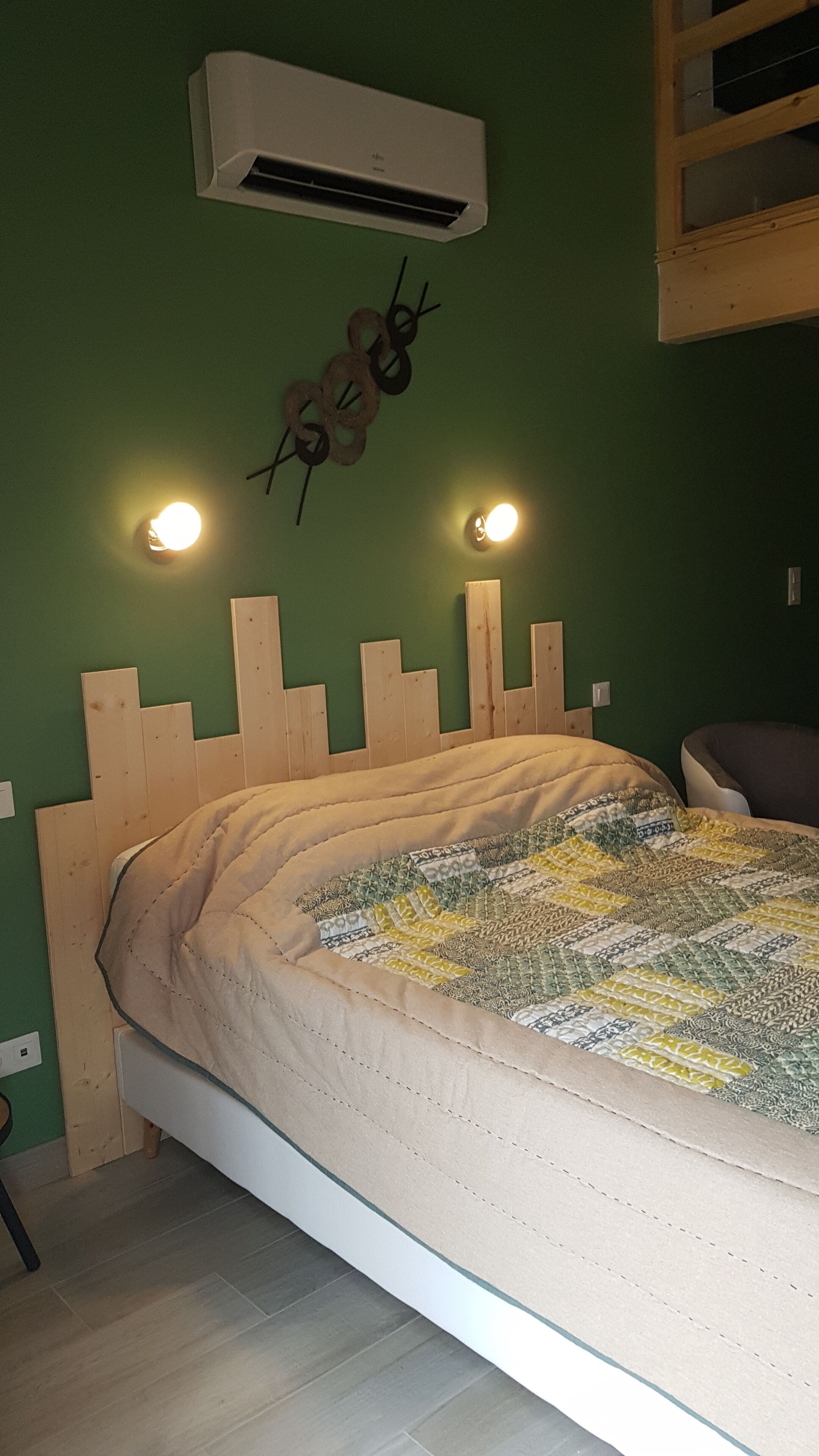 A bedroom with a wooden headboard, a quilted bedspread, an air conditioner, and wall-mounted lights.
