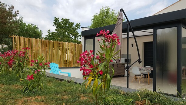 Un espacio exterior moderno con una estructura de vidrio, valla de bambú y una silla azul.