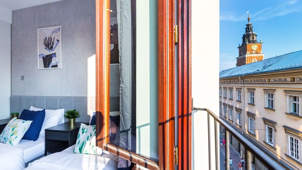 Ein Hotelzimmer mit Bett, Nachttischen und Blick auf ein historisches Gebäude mit einem Glockenturm.