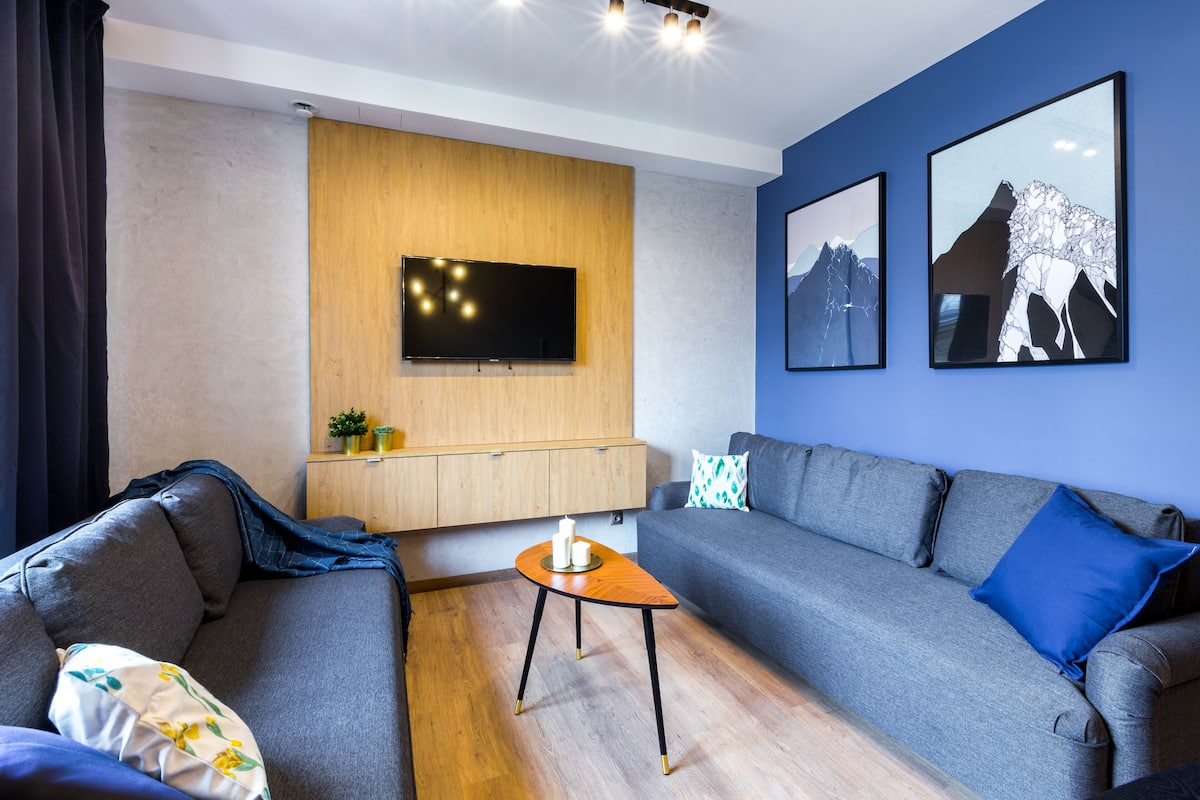 A modern living room with a grey sofa, a wooden cabinet, a TV mounted on the wall, and two framed pictures.