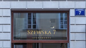 Der Eingang zu den Apartments Szepska 7 mit einer deutlichen Beschilderung über der Tür, einem gefliesten Boden und einer Backsteinwand.