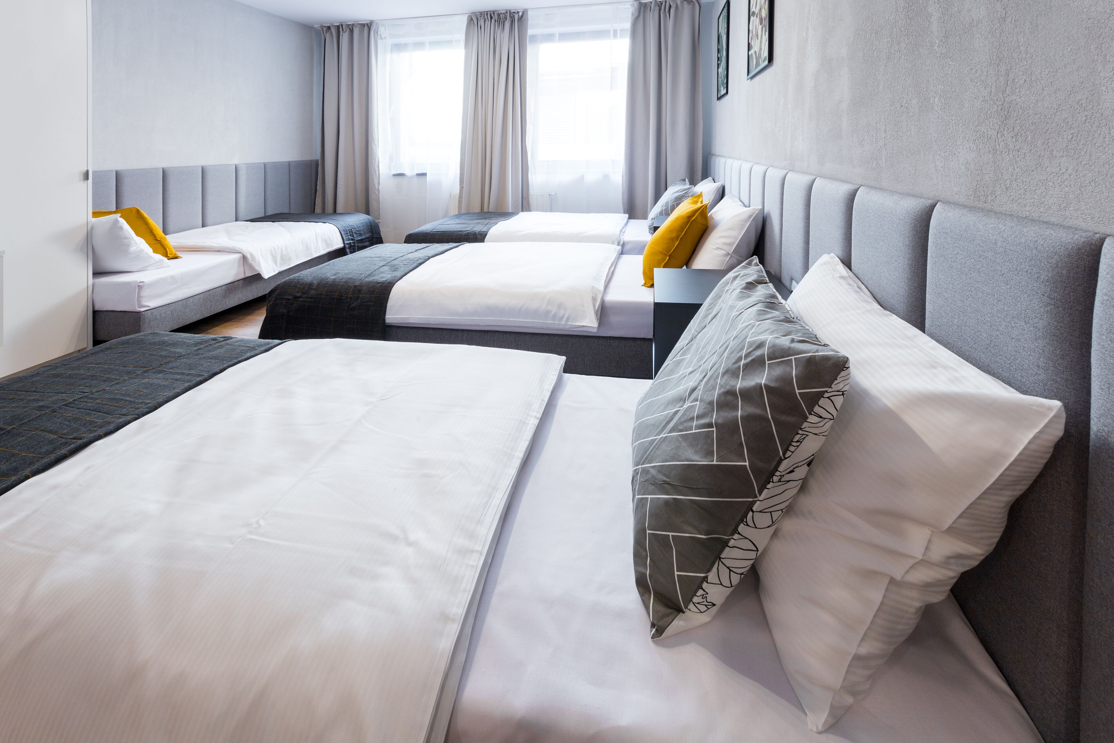 Habitación de hotel con dos camas, un cabecero gris y una ventana con cortinas.