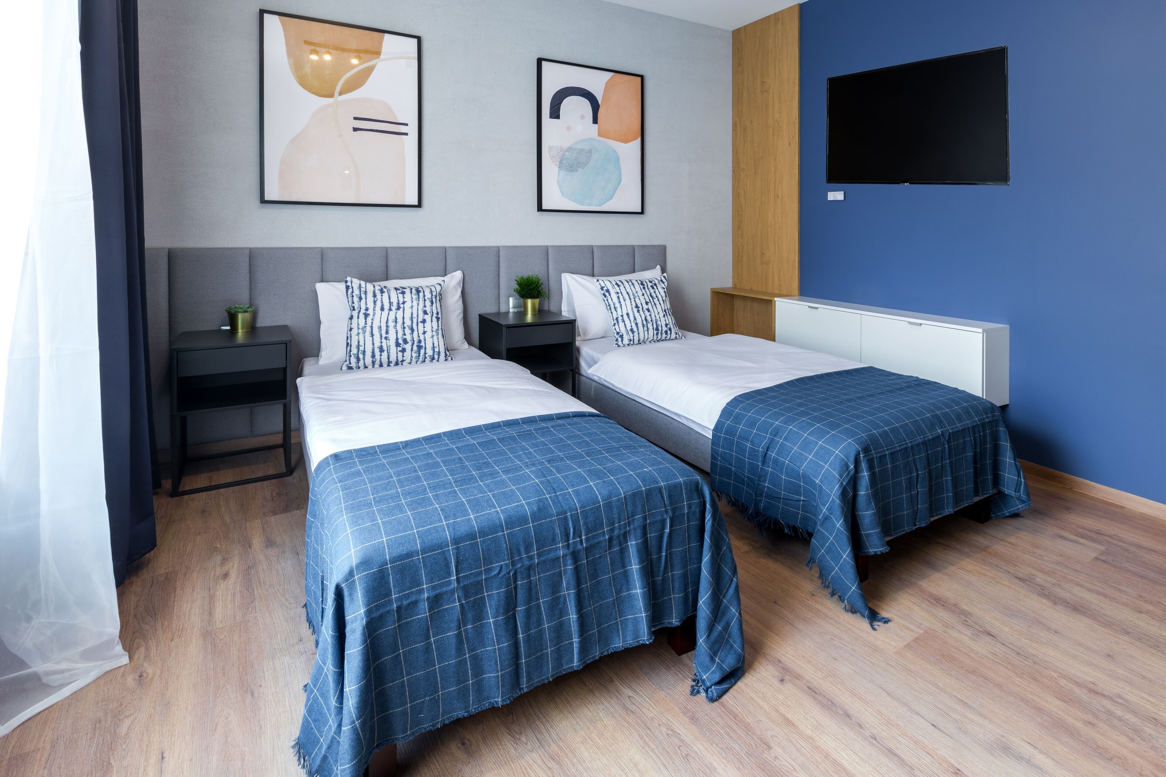 A hotel room with two beds, a TV, artwork on the wall, and a wooden floor.