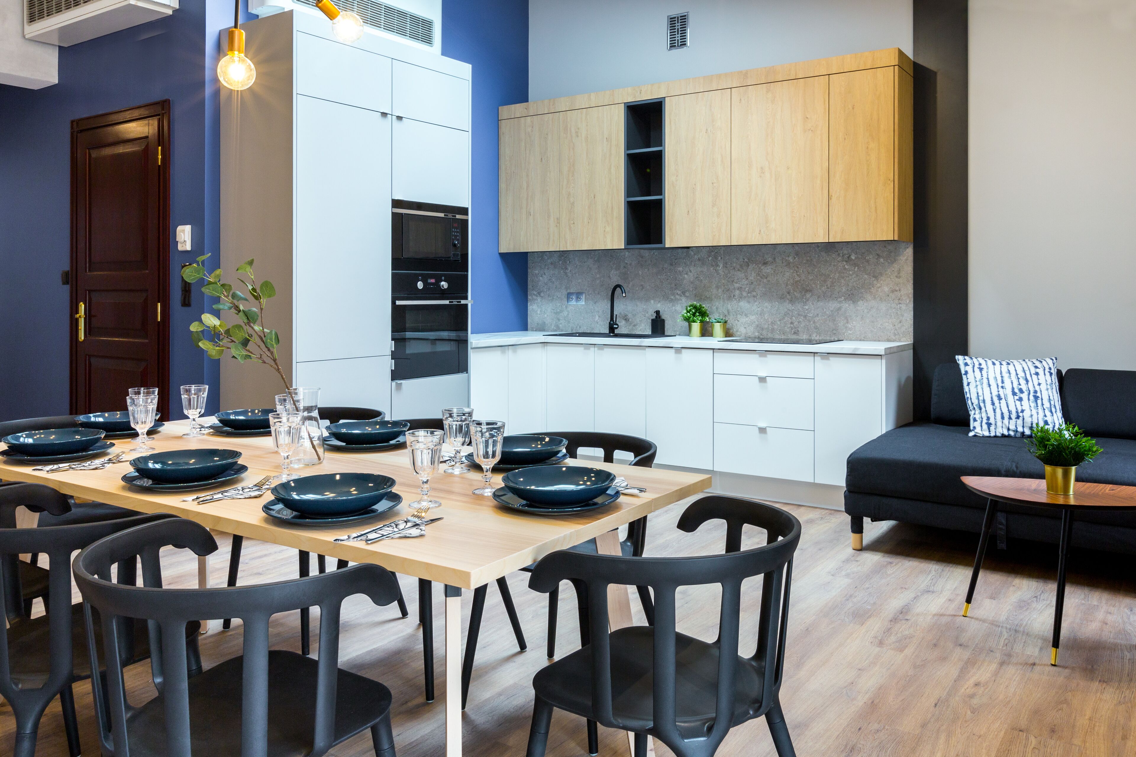A modern kitchen with white cabinets, a wooden countertop, and a dining area with a wooden table and black chairs.