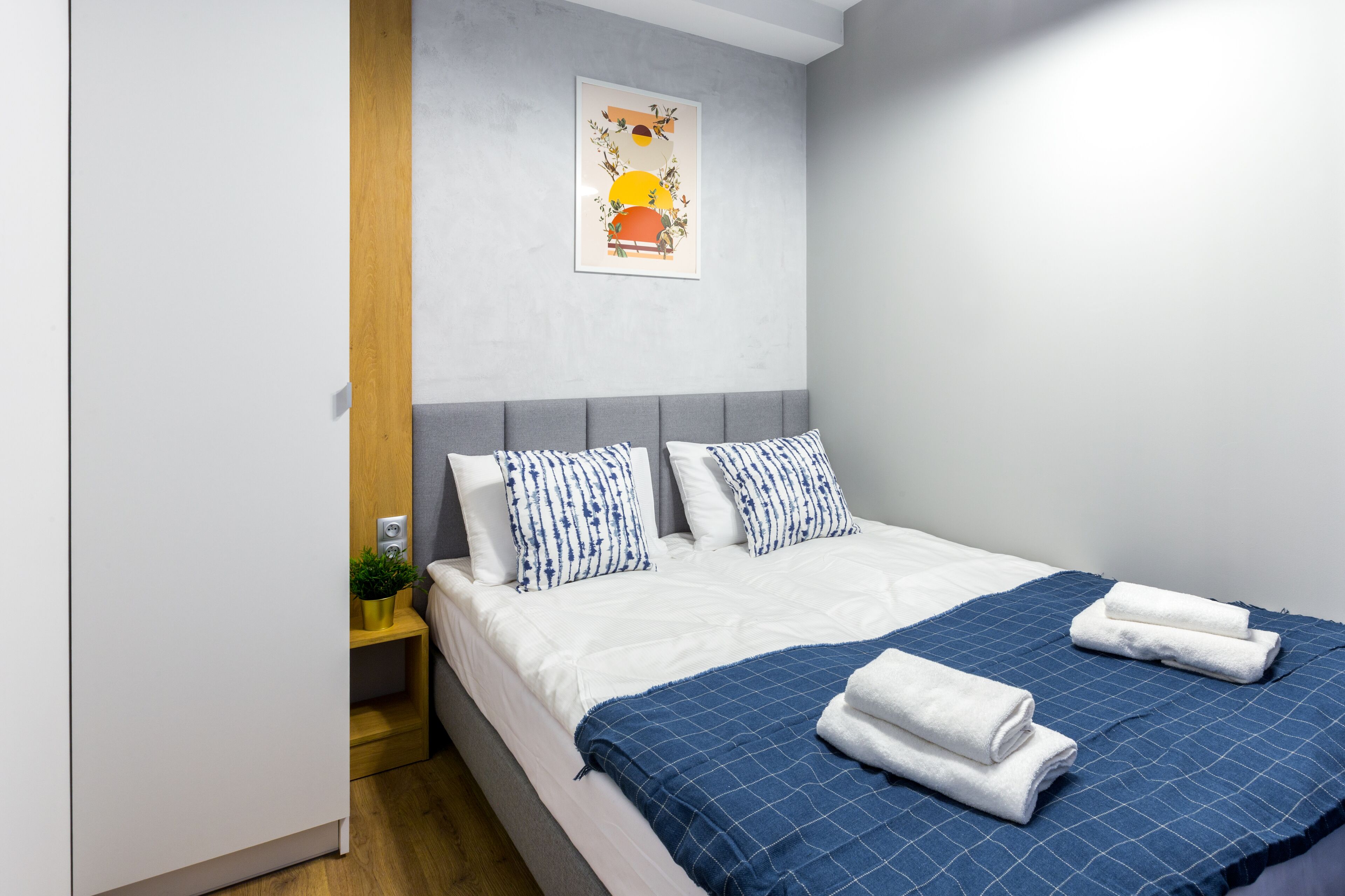 A neatly made bed with blue and white bedding, a blue blanket, and two rolled towels.