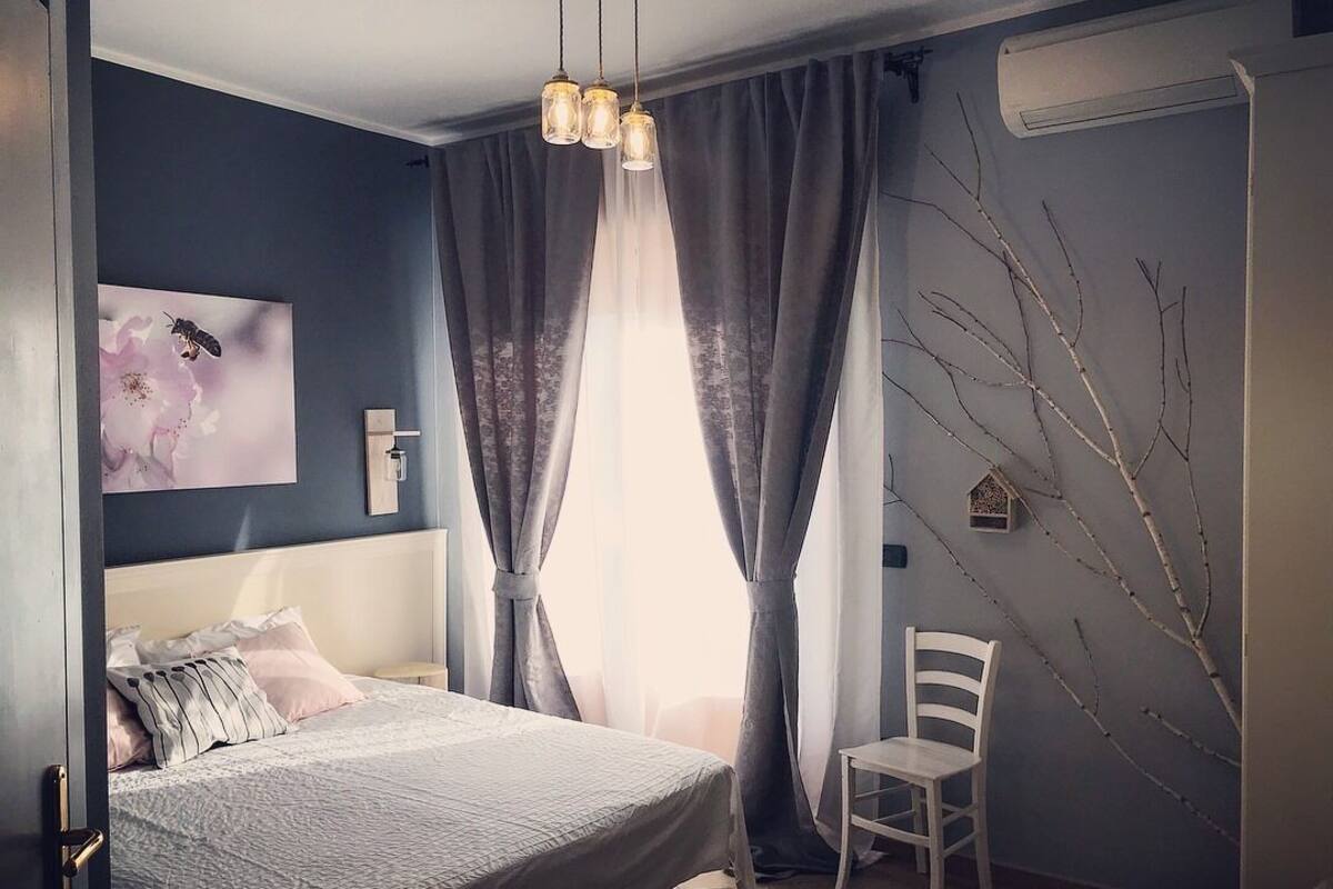 Een slaapkamer met een bed, een stoel, een wandairconditioner en een raam met gordijnen.