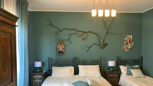 Une chambre avec deux lits, une armoire en bois, une décoration murale en forme de branche et un luminaire suspendu.