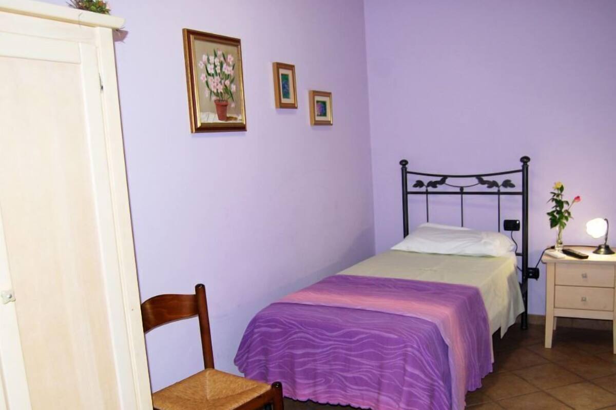 Een slaapkamer met een bed, een stoel, een nachtkastje en een kapstok.
