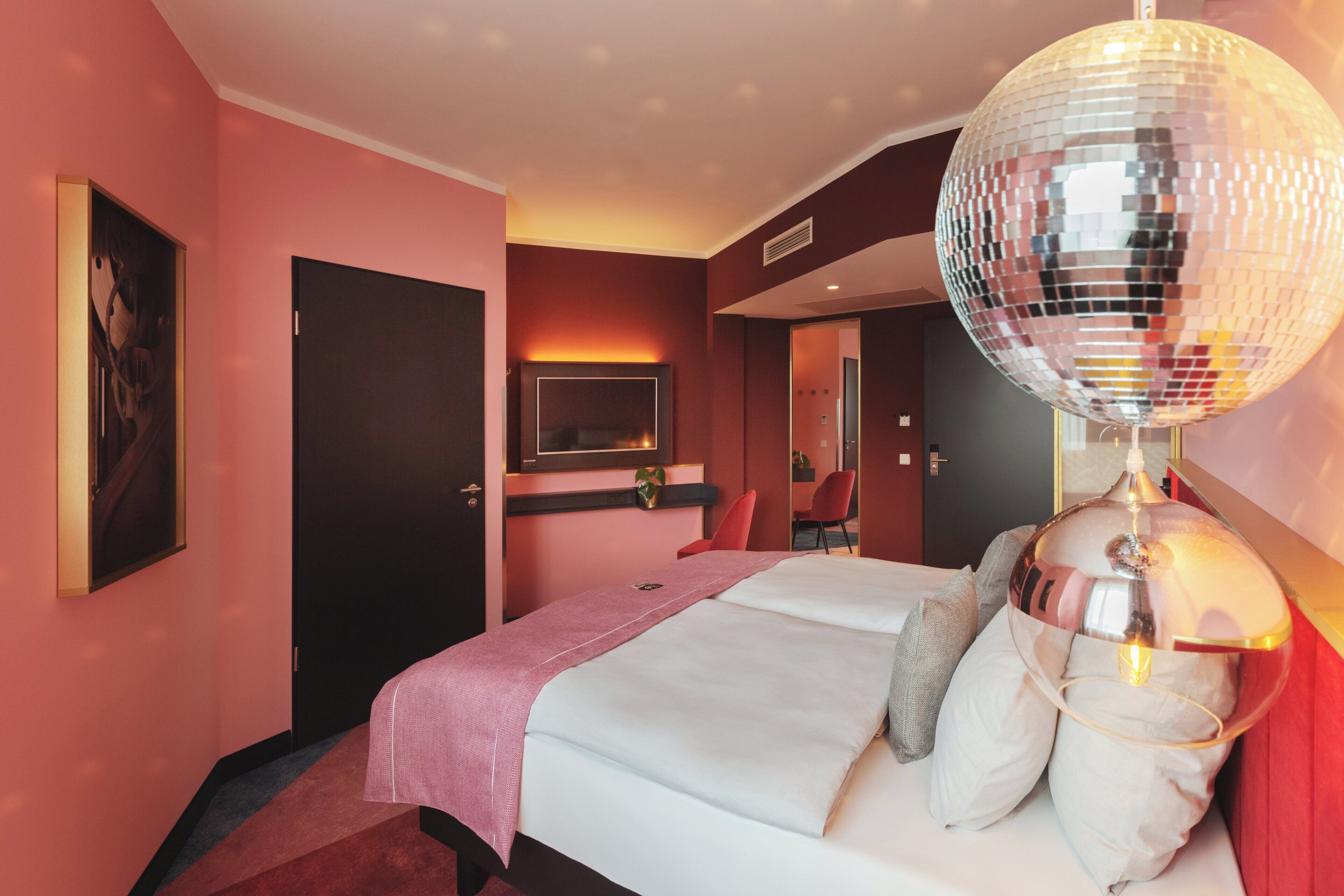 A hotel room with a bed, a disco ball, a TV, and a red chair.