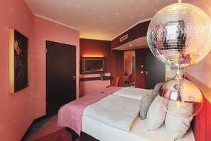 A hotel room with a bed, a disco ball, a TV, and a red chair. - Holiday Inn - the niu, Loco Munich North by IHG (Munich)