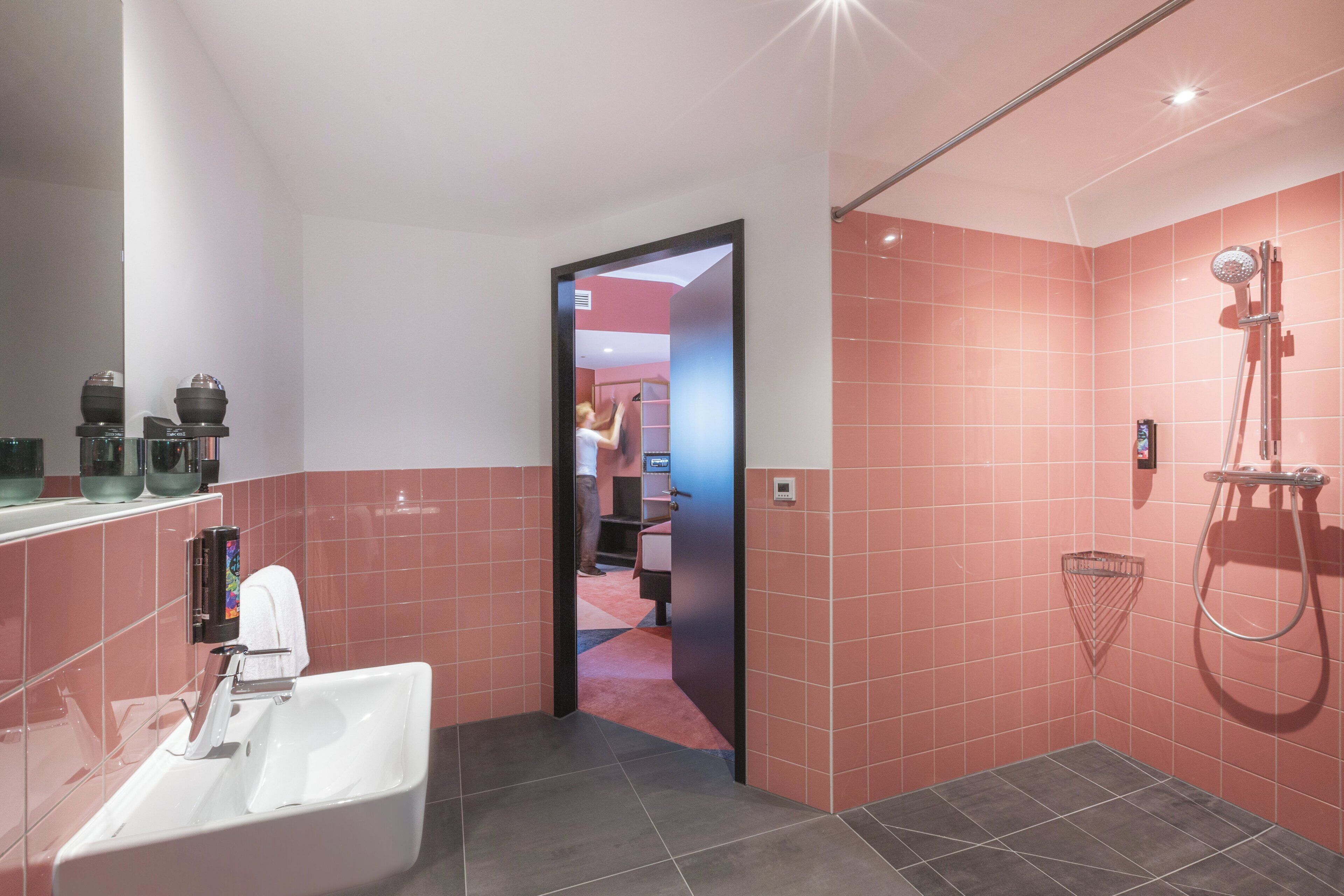 A modern bathroom with a large sink, a shower, and pink tiled walls.