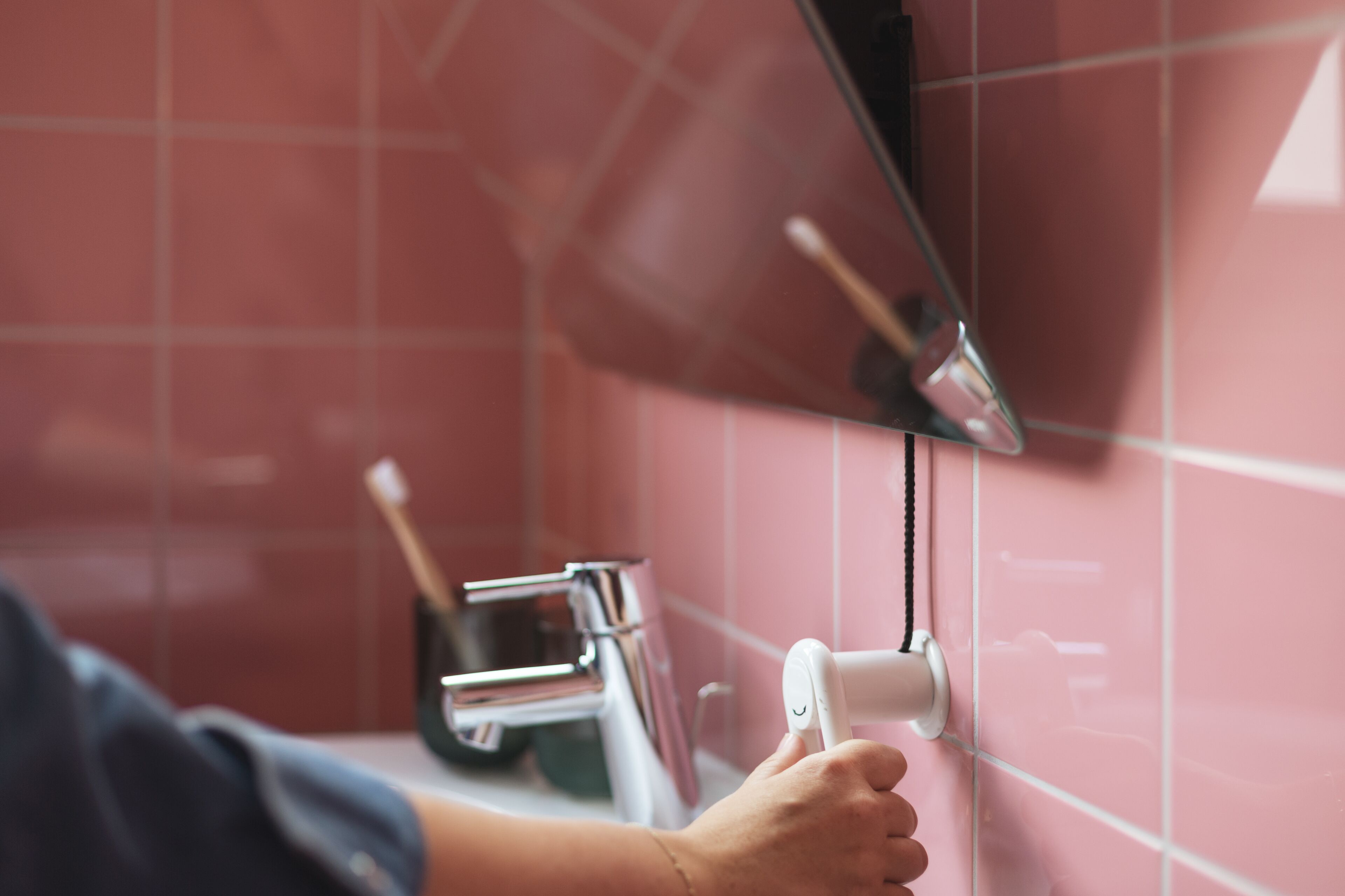 Una mano ajustando un dispensador de toallas fijado en una pared de azulejos.