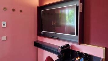A hotel room with a TV mounted on a dark wall, a coffee machine, and a tray with cups and a small box.