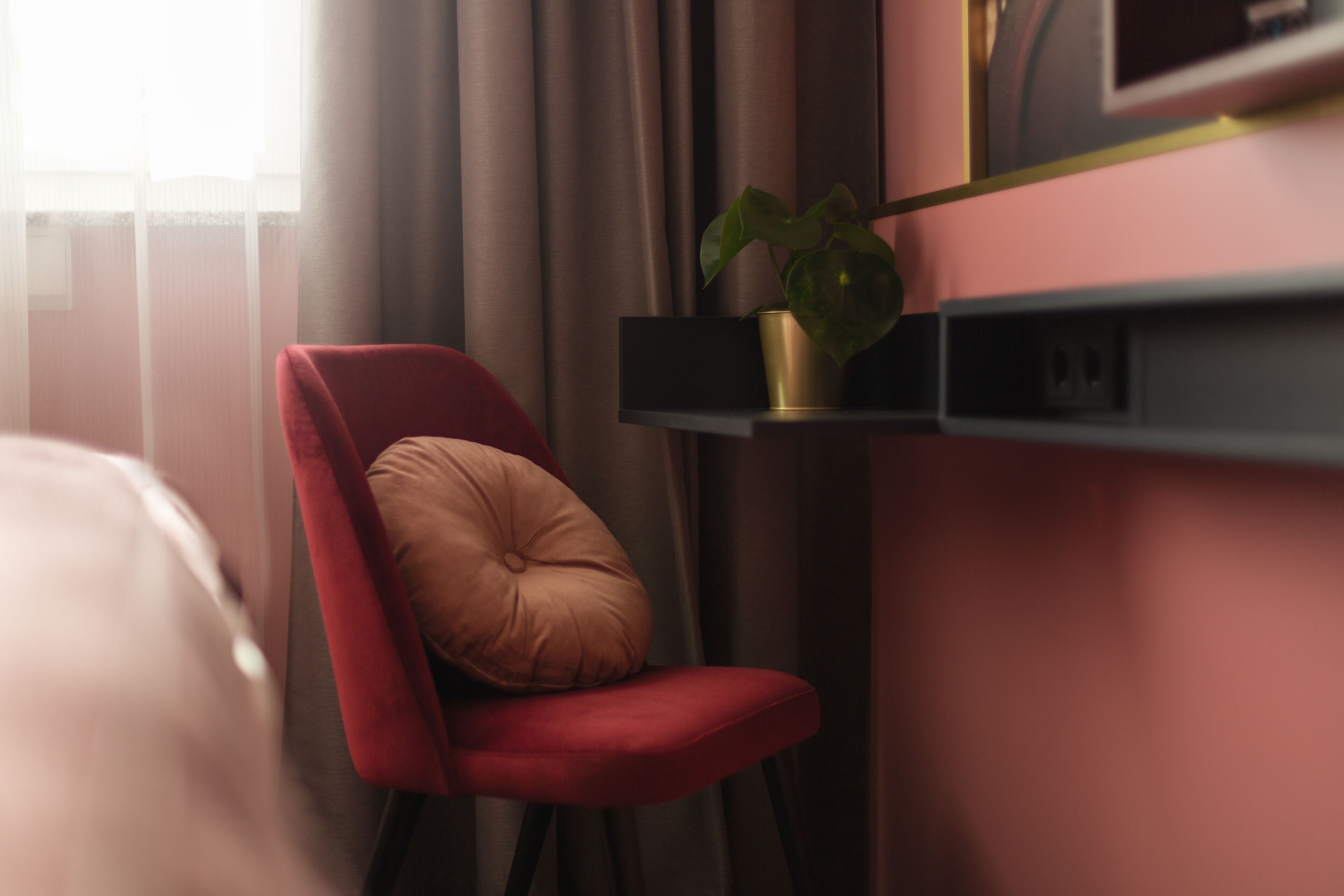 A modern room with a red chair, a small plant on a shelf, and a television on the wall.