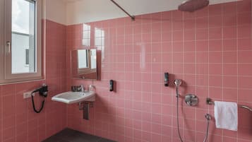 A bathroom with pink tiles, a sink, a mirror, a shower, and a towel rack.
