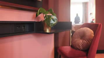 A modern hotel lobby with a red chair, a plant on a shelf, and a person in the background.