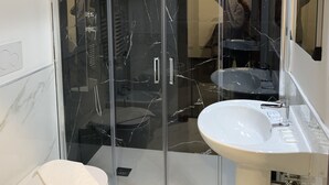 A modern bathroom with a glass-enclosed shower, a white sink, and a marble-tiled floor. - Lungotevere Collection Suite (Rome)