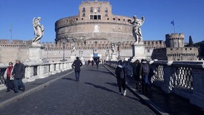 A stone bridge with statues on either side, leading to a large historic building with a round central tower. - Lungotevere Collection Suite (Rome)