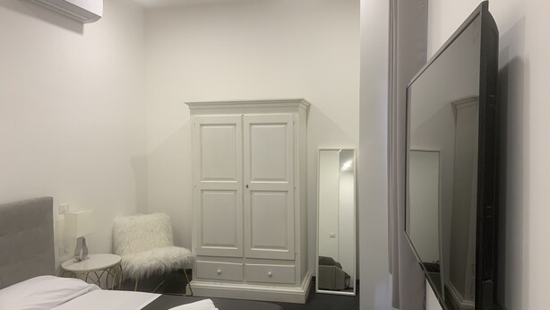 A hotel room with a bed, a wardrobe, a TV, and a small round table. - Lungotevere Collection Suite (Rome)