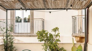 A covered patio with a table set for two, surrounded by potted plants and outdoor furniture. - Balate Dimora In Centro (Ragusa)