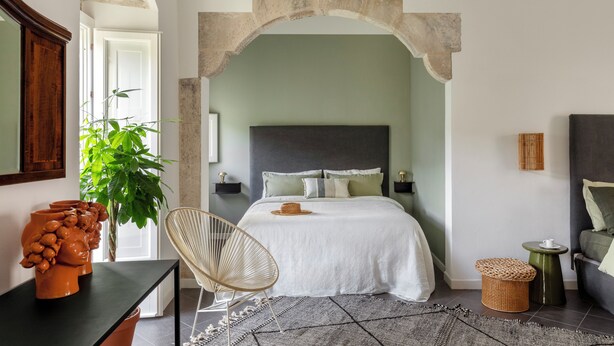 A bedroom with a bed, a chair, a small table, and a potted plant. - Balate Dimora In Centro (Ragusa)